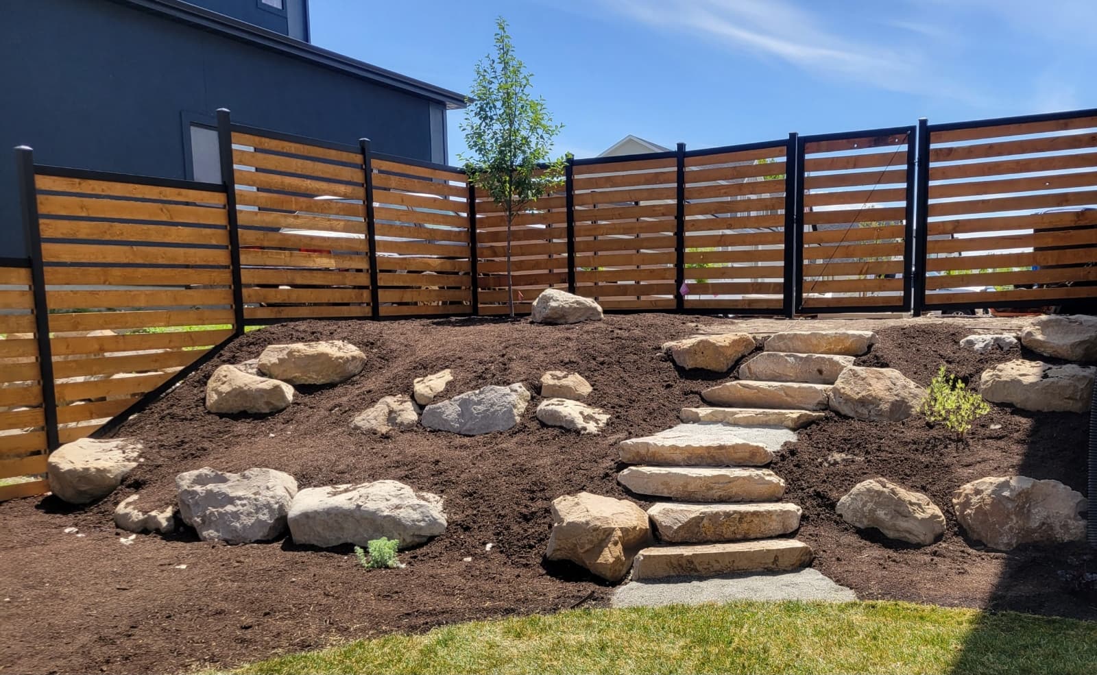 Horizontal slat fence on a mulched slope by SG Landscaping
